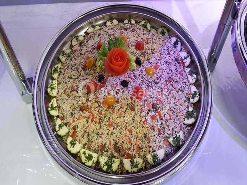 Plat rond de taboulé garni de tomates cerises, rondelles de concombre, olives et décoré d'une rose en tomate.