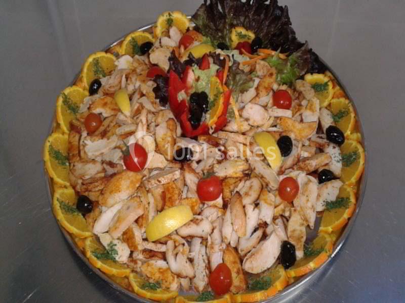 Assiette garnie de morceaux de poulet, tranches d'orange, tomates cerises, olives noires et décoration de légumes.