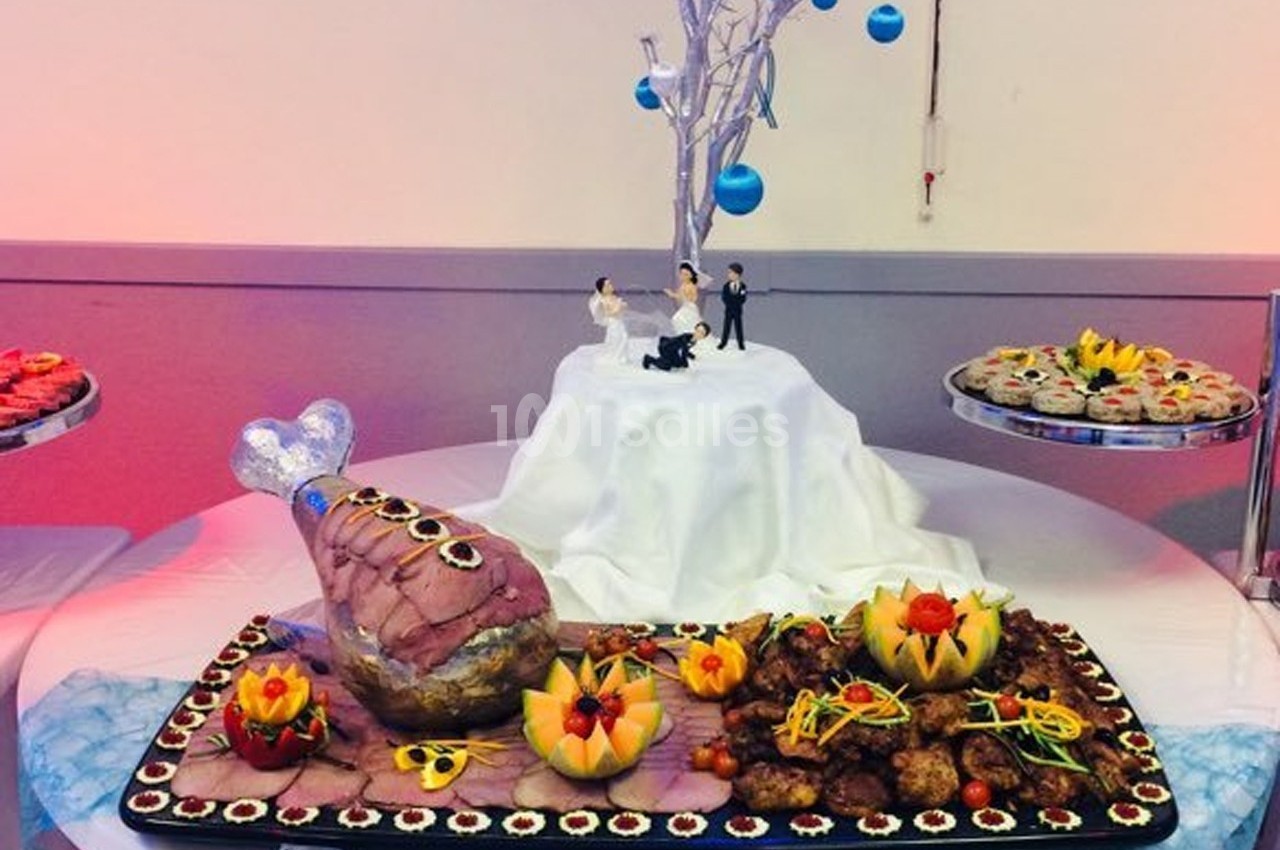 Plateau de buffet décoratif avec viande, fruits sculptés et figurines de mariage sur une table ornée.
