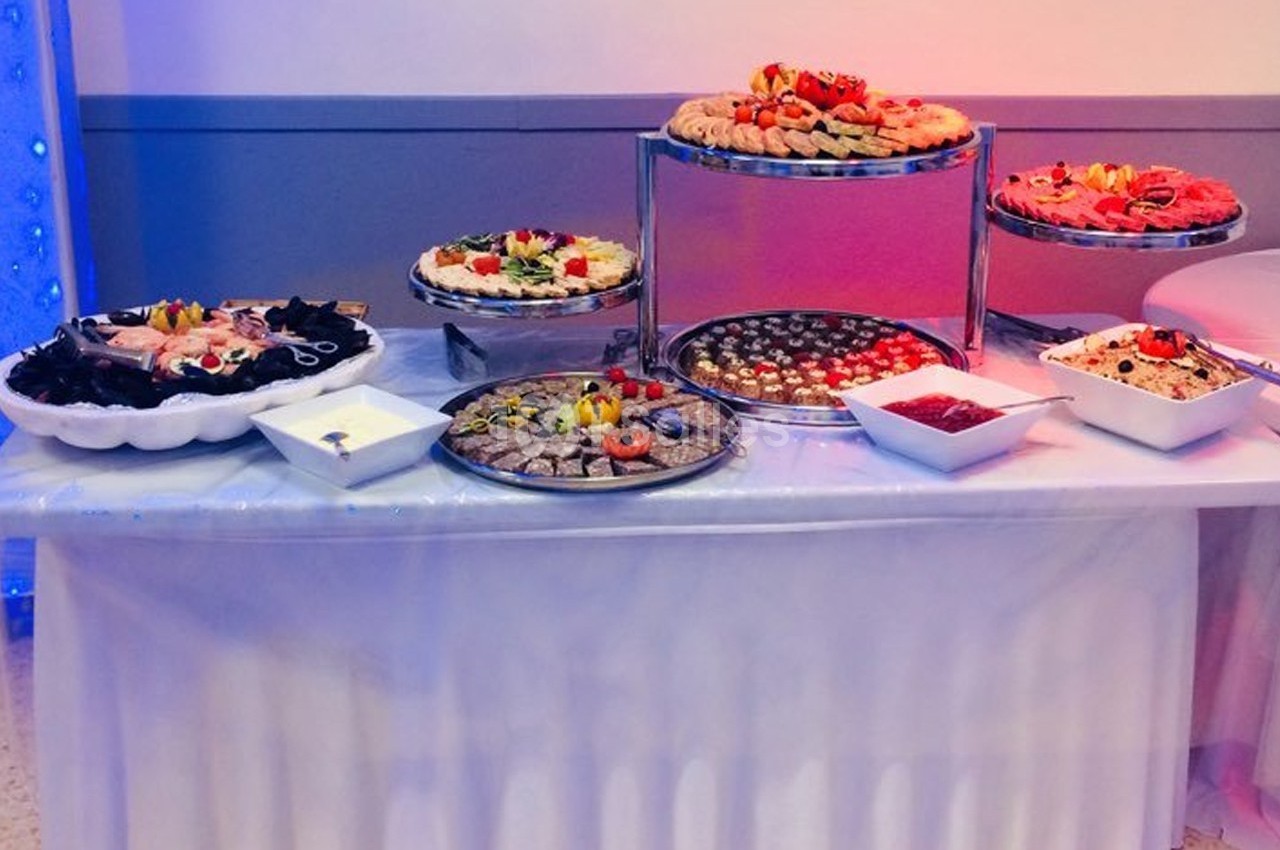 Table de buffet avec divers plats, notamment des plateaux de desserts, fruits, sauces et amuse-bouches.