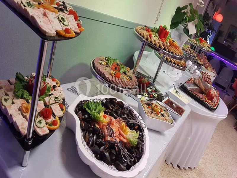 Buffet varié avec fruits de mer, charcuteries, salades et amuse-bouches disposés sur des plateaux et une table blanche.
