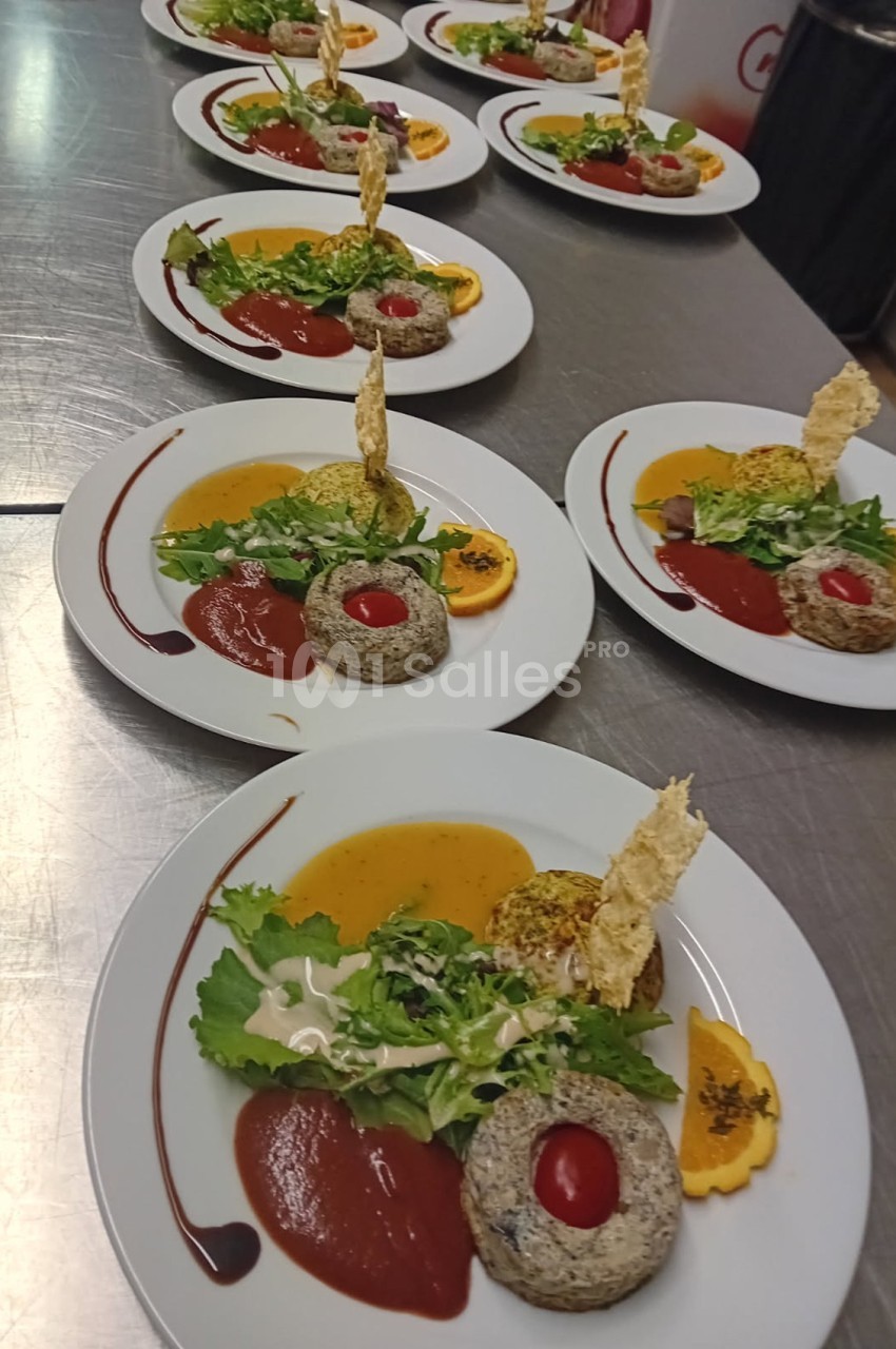 Assiettes dressées avec des portions de légumes, purées, sauces et décorations croustillantes sur une table en inox.