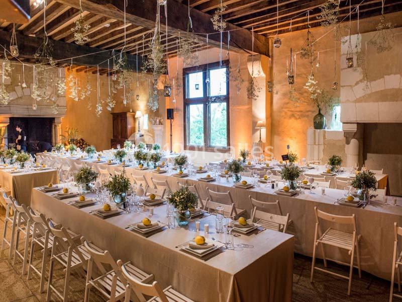 Salle de réception décorée avec des tables alignées, nappes blanches, chaises pliantes et ornements suspendus.