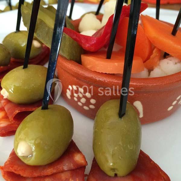 Olives vertes, tranches de chorizo et légumes marinés présentés sur des piques, avec un bol en terre cuite en arrière-plan.