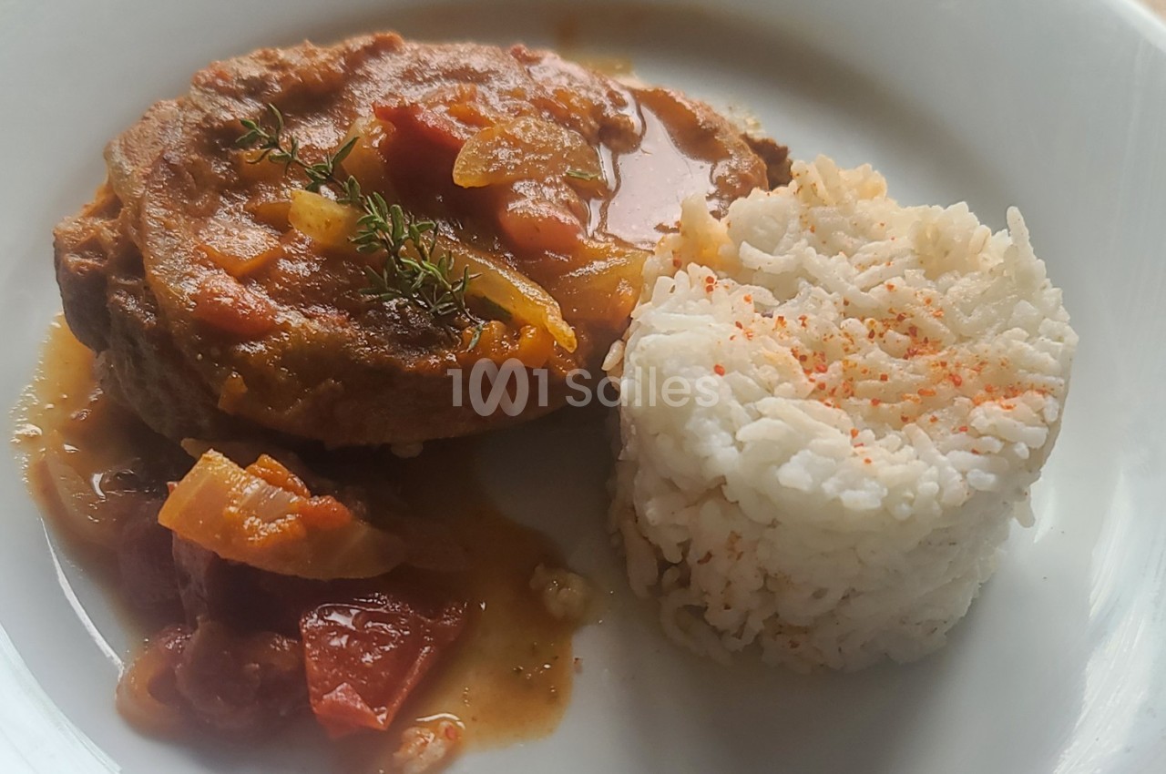 Assiette contenant une tranche de viande en sauce avec des légumes et un accompagnement de riz blanc saupoudré de paprika.