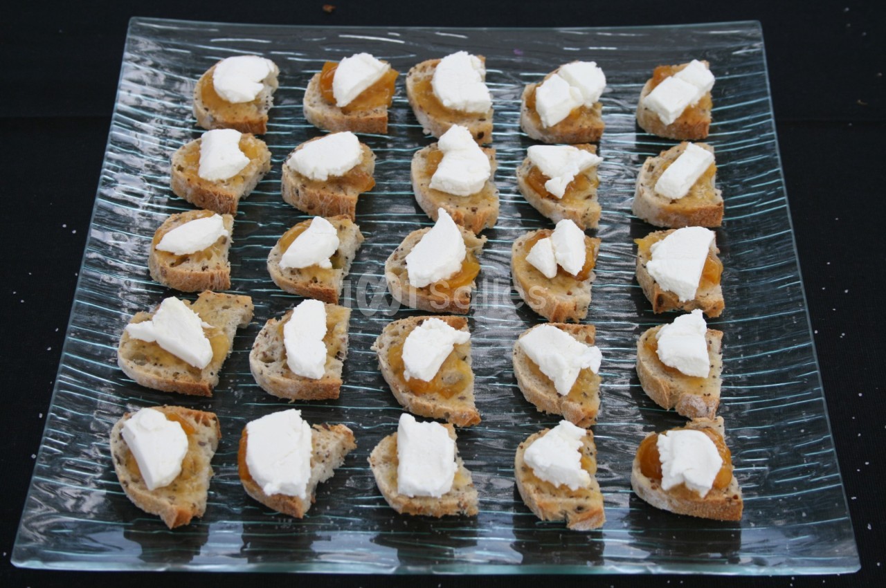 Tranches de pain garnies de fromage blanc et de confiture, disposées en rangées sur un plateau en verre.