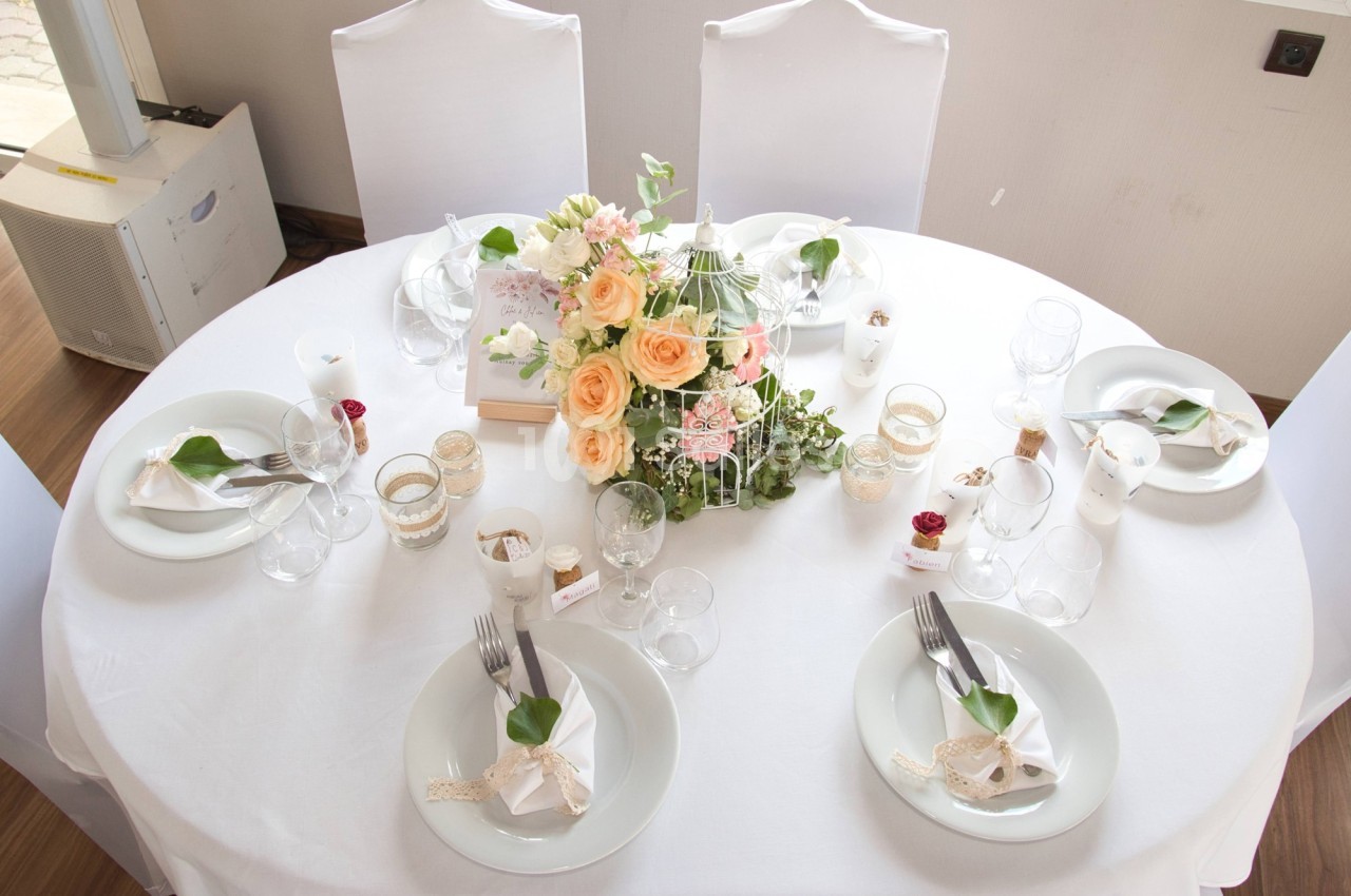 Table ronde décorée pour un mariage avec des fleurs, des bougies et des serviettes pliées sur des assiettes blanches.