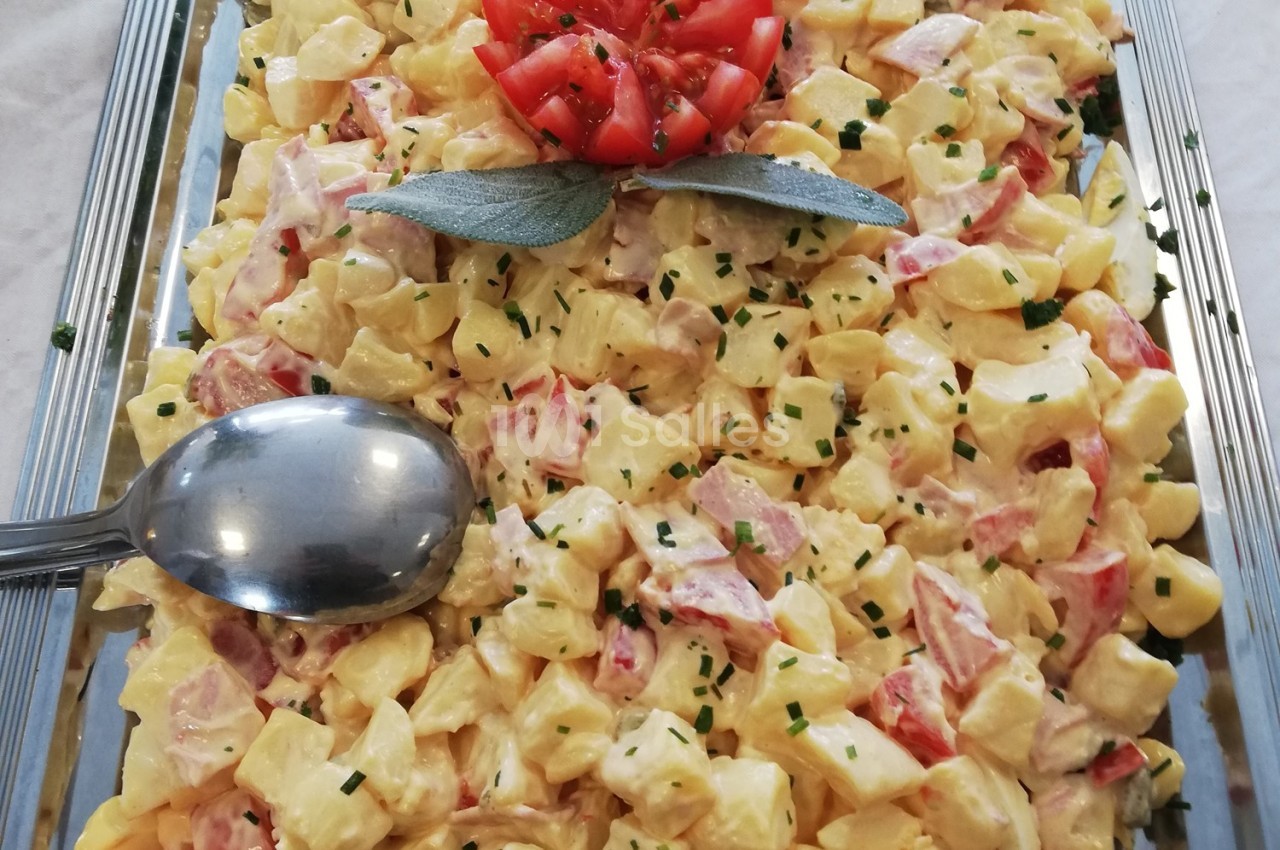 Salade de pommes de terre avec morceaux de tomates, ciboulette et mayonnaise, décorée d'une fleur de tomate.