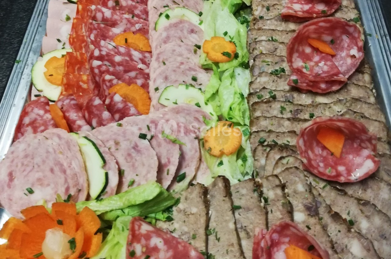 Plateau de charcuterie variée avec salami, pâté, légumes décoratifs et feuilles de salade.