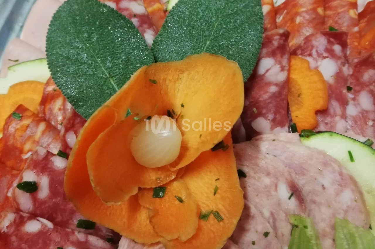 Tranches de charcuterie décorées avec une fleur en carotte, une feuille de sauge et un petit oignon au centre.