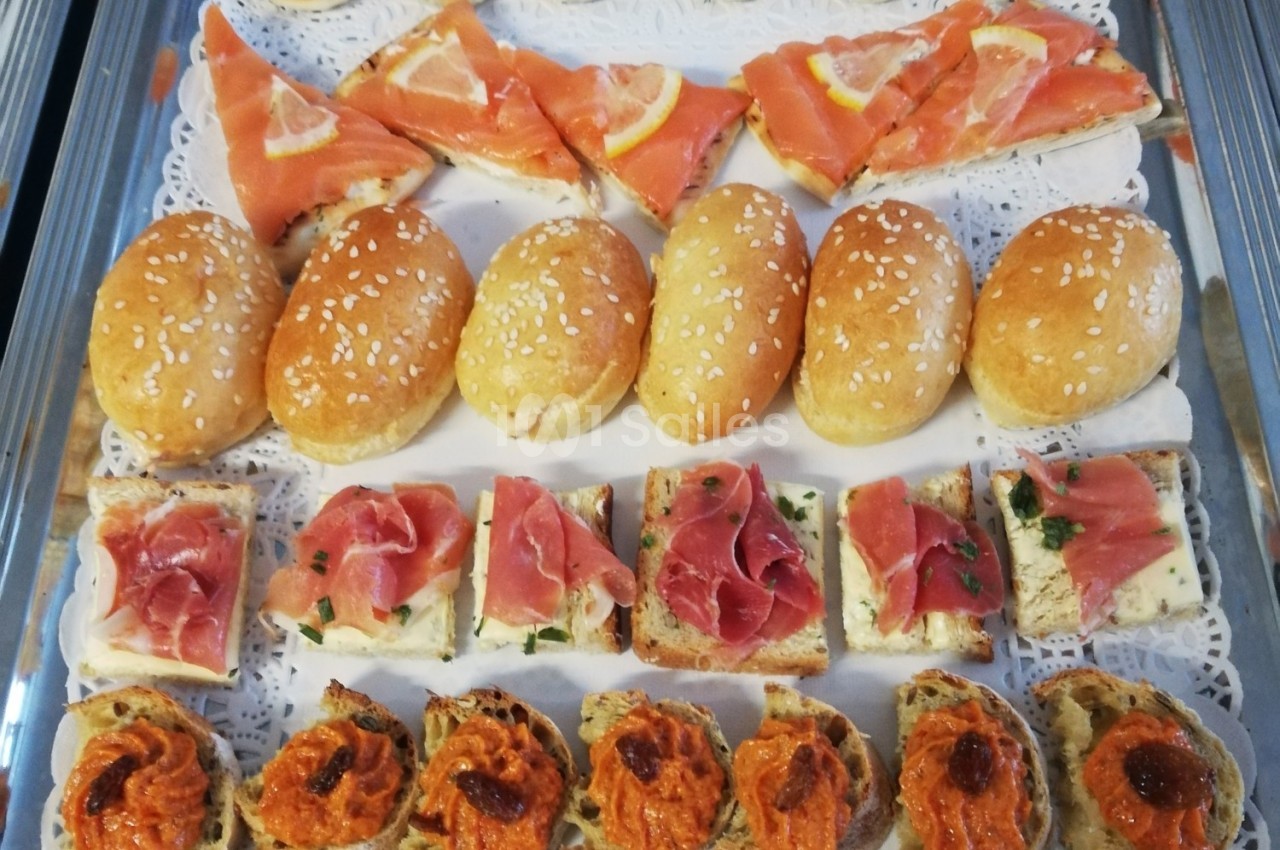 Plateau de canapés variés avec saumon, jambon cru, tapenade et petits pains au sésame sur nappe blanche.