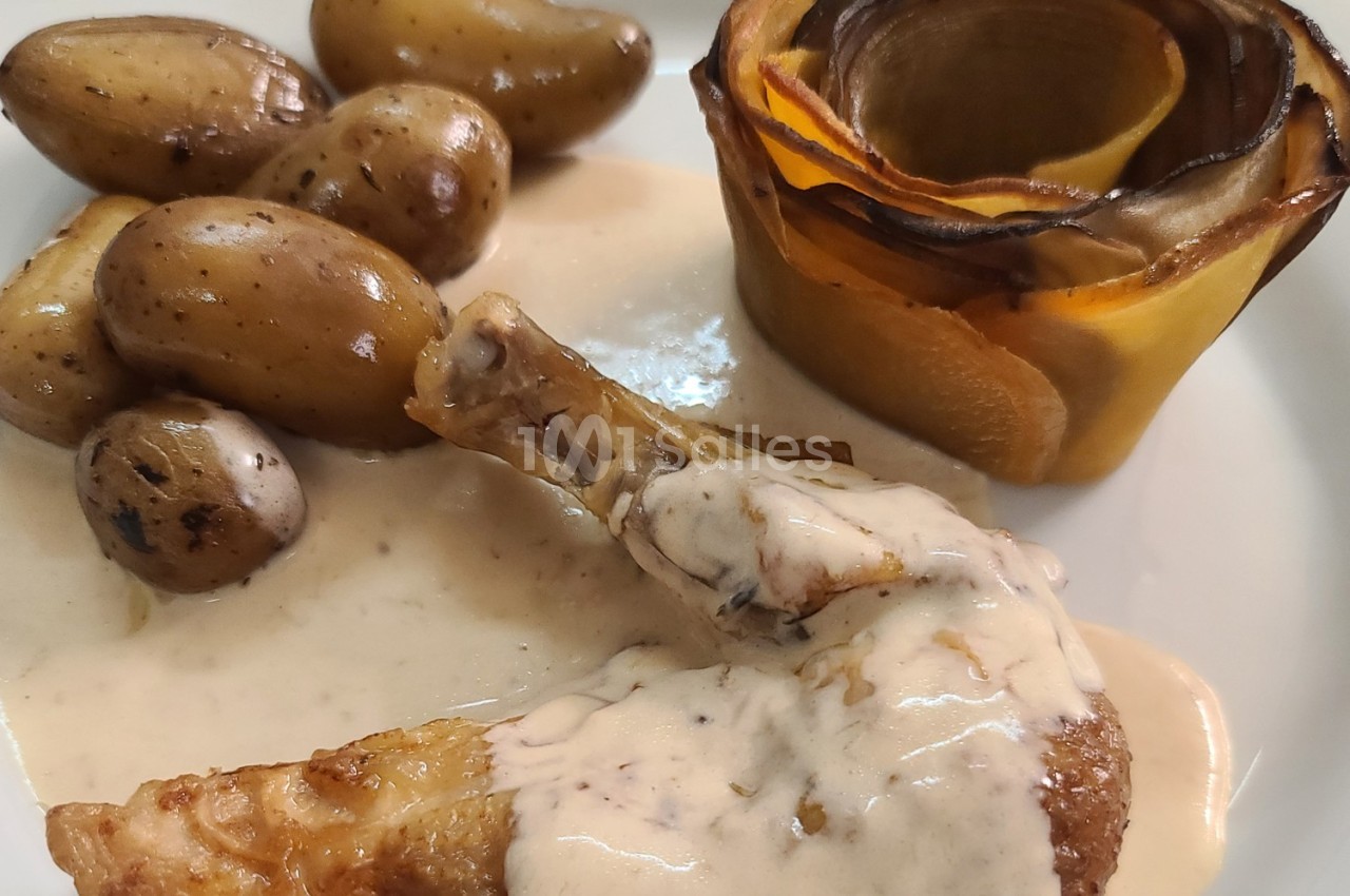 Plat composé d'une cuisse de volaille nappée de sauce, pommes de terre rôties et roulé de légumes en forme de fleur.