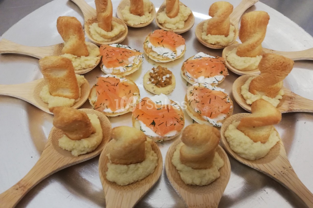 Assortiment d'amuse-bouches sur plateau, avec cuillères en bois garnies et toasts au saumon fumé.