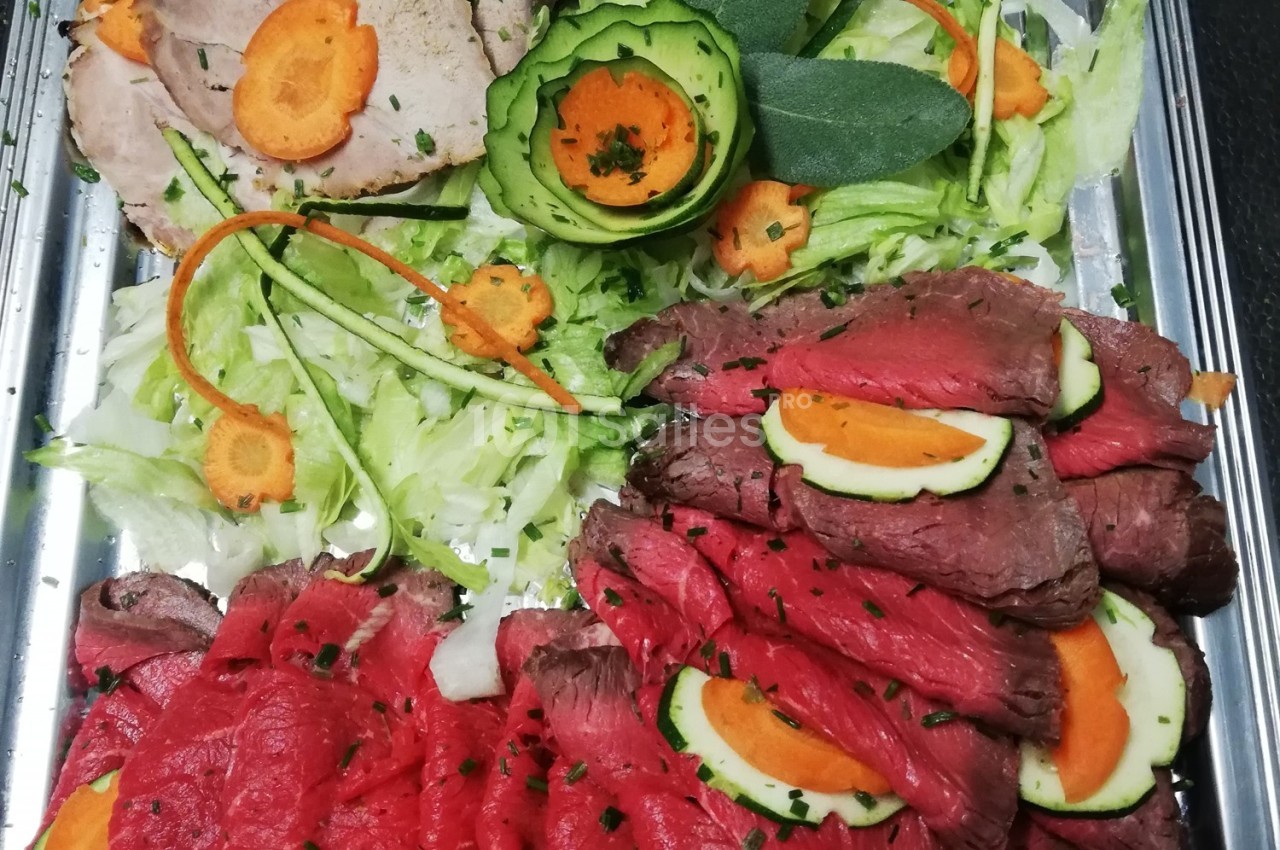 Plateau de viande froide avec tranches de rôti de bœuf et de porc, décoré de légumes frais et herbes.