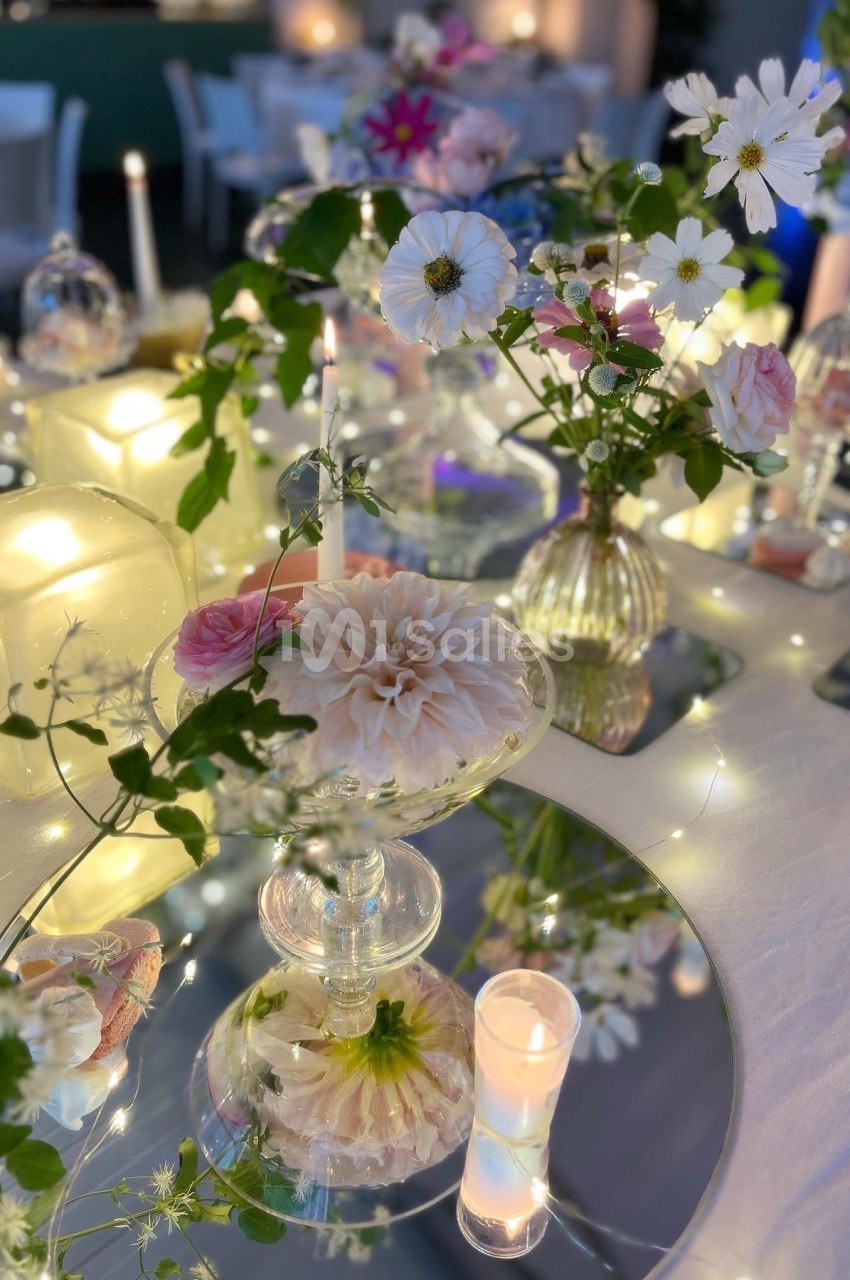 Arrangement floral élégant avec bougies, miroirs et guirlandes lumineuses sur une table décorée.