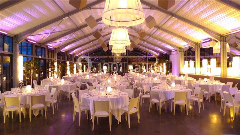 Salle de réception élégante avec tables rondes dressées, éclairage tamisé et lustres suspendus.