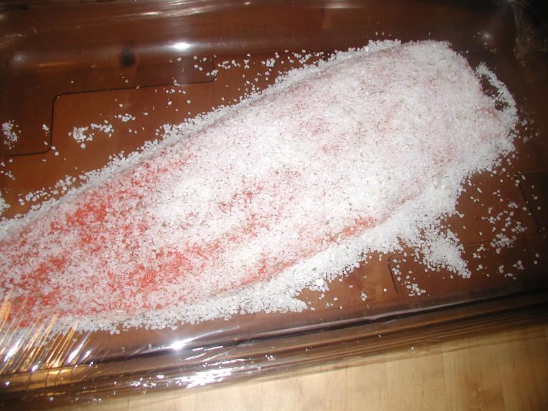 Filet de poisson recouvert de sel dans un plat transparent, prêt pour une préparation culinaire.