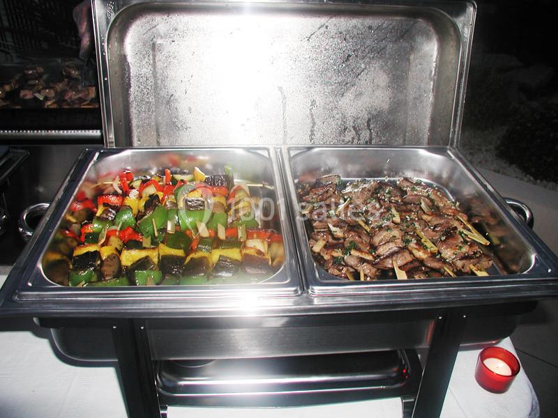 Plateaux en inox contenant des brochettes de légumes colorés et des morceaux de viande grillée, présentés sur un buffet.