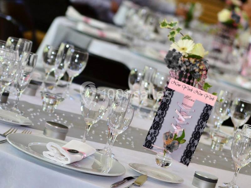 Table dressée pour un événement avec nappes blanches, verres, couverts, menu décoratif et centre de table floral.