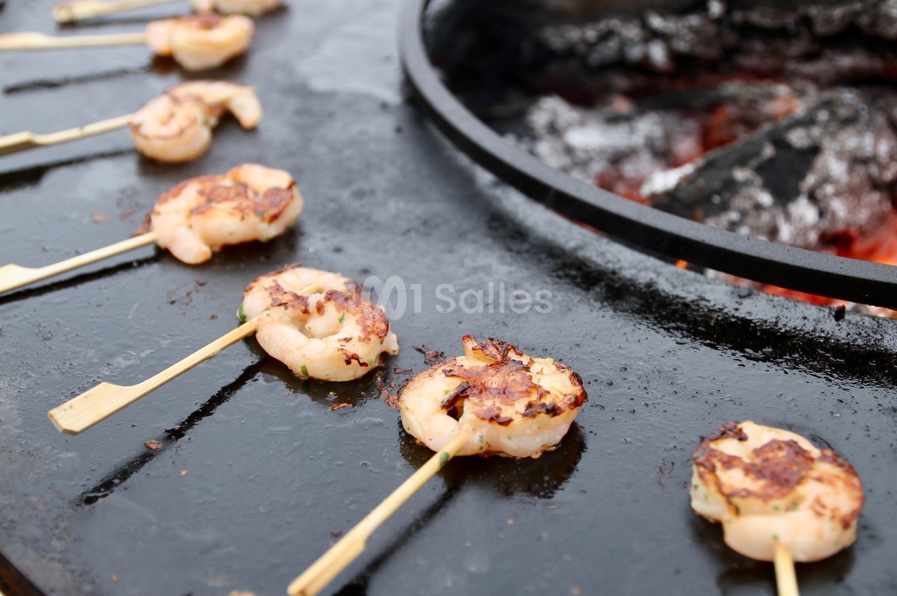 Brochettes de crevettes grillées sur une plaque de cuisson ronde au-dessus de braises.