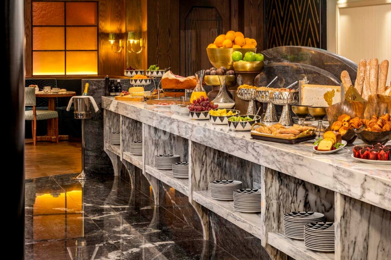 Buffet avec fruits, viennoiseries, pains, charcuterie et plats variés sur un comptoir en marbre dans une salle élégante.