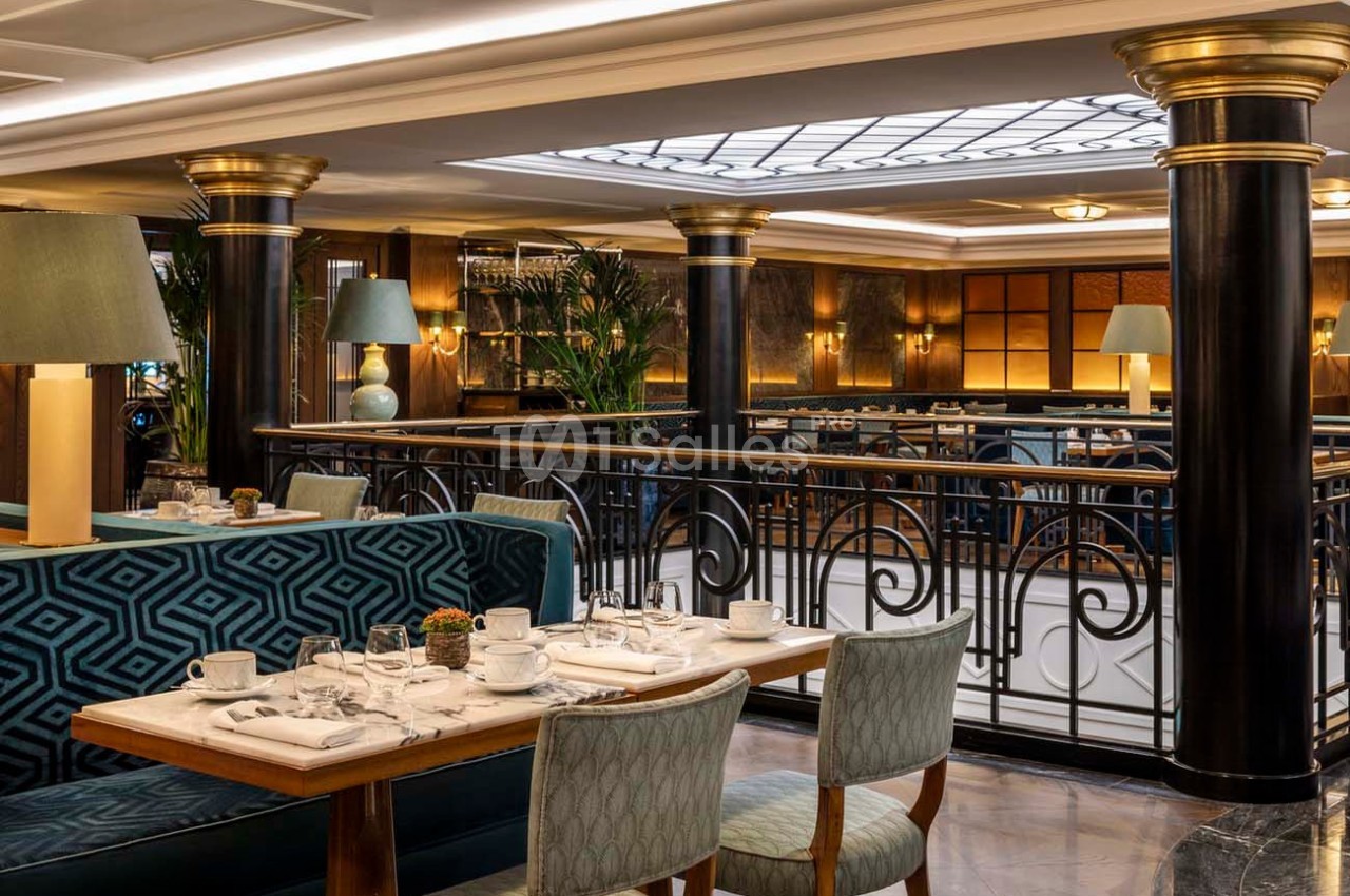 Salle de restaurant élégante avec tables dressées, banquettes en velours bleu et colonnes noires ornées de détails dorés.