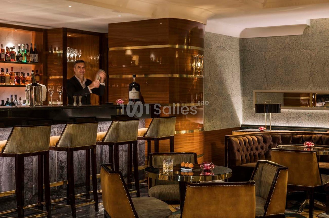 Un barman prépare un cocktail derrière un comptoir dans un bar élégant avec des tables et des fauteuils en cuir.