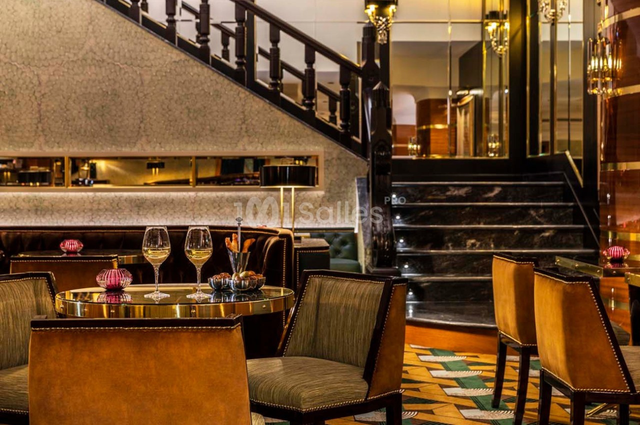 Salle de restaurant élégante avec table dressée, chaises en cuir, escalier en marbre et éclairage chaleureux.