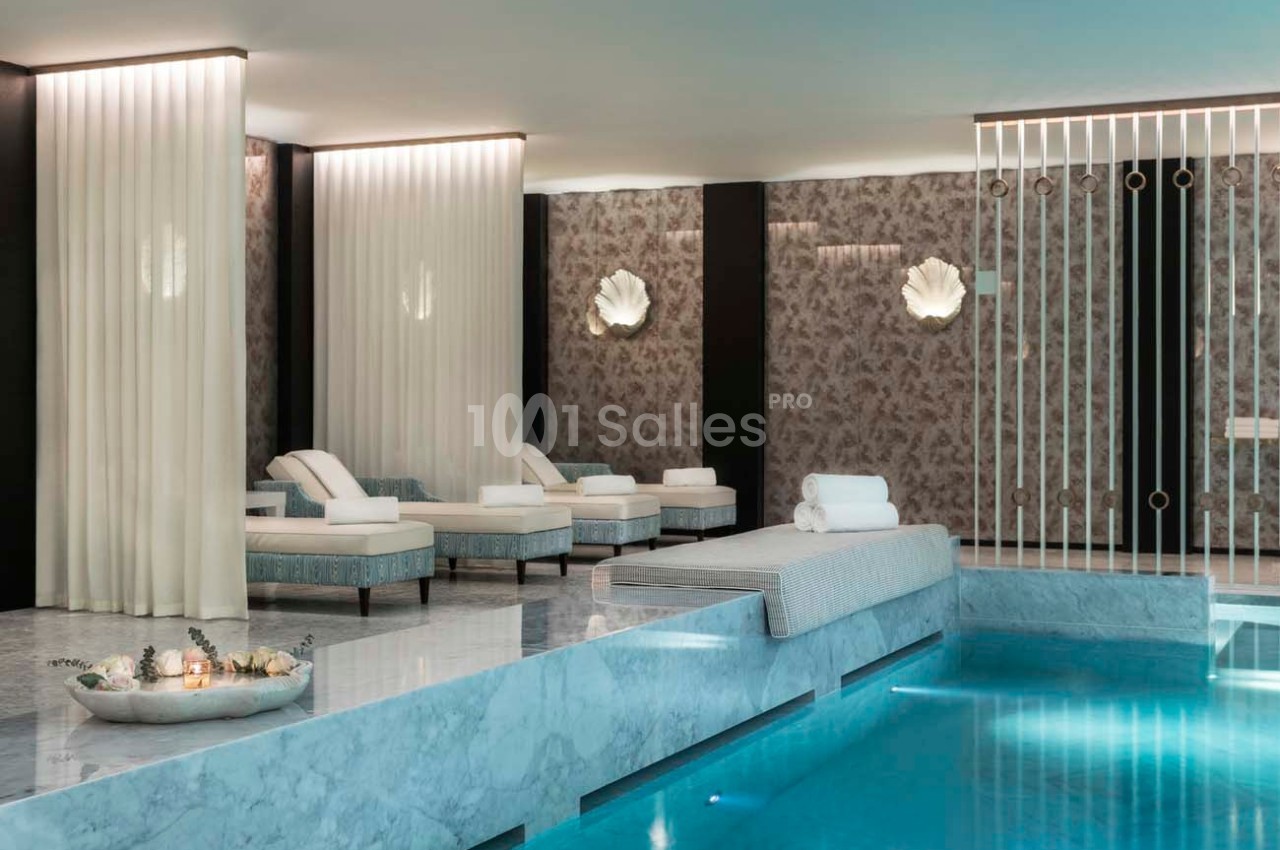 Espace spa avec piscine intérieure, lits de repos, rideaux blancs et éclairage tamisé.