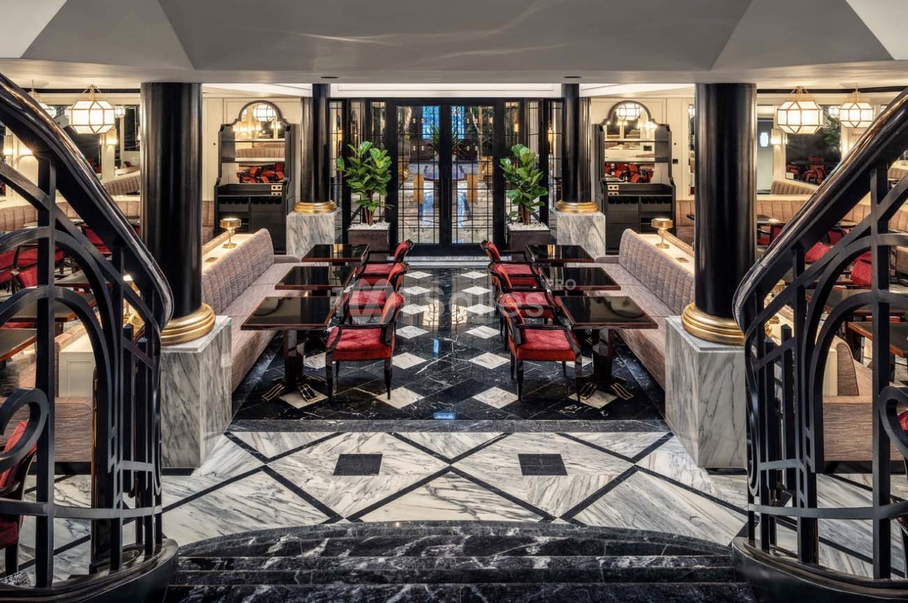 Salle de restaurant élégante avec tables noires, chaises rouges, sol en marbre et décoration raffinée.