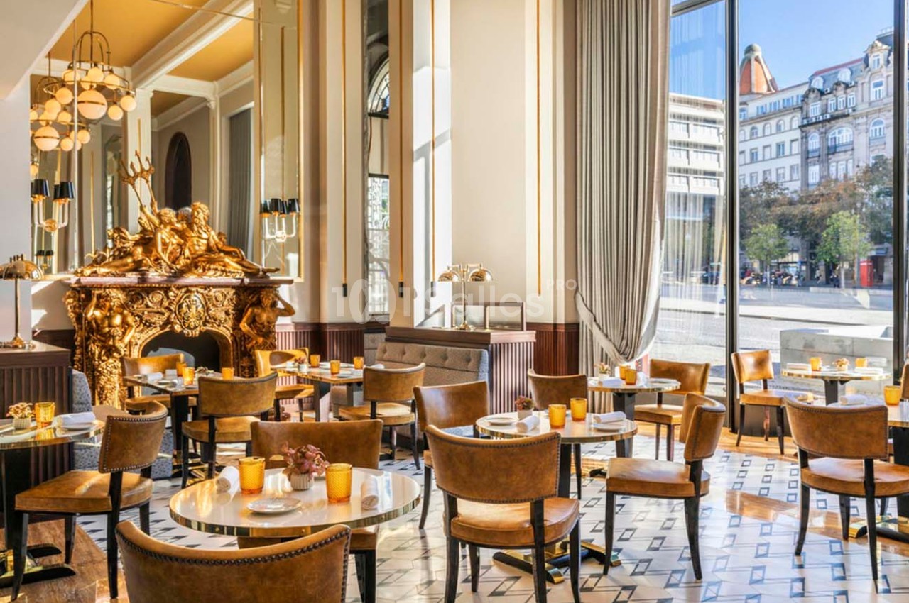 Salle de restaurant élégante avec mobilier en cuir, cheminée dorée ornée et grandes baies vitrées donnant sur la ville.