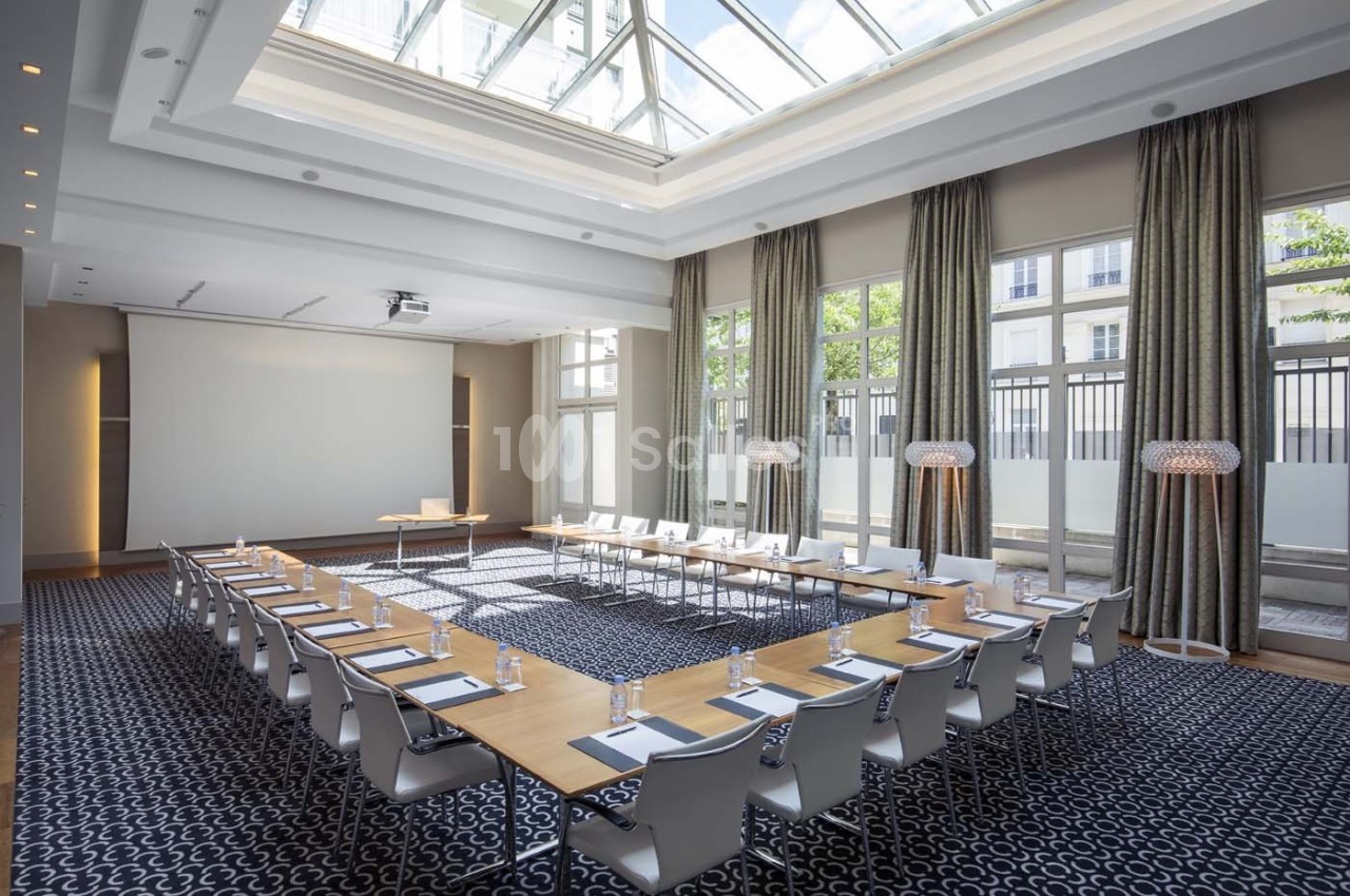 Salle de réunion lumineuse avec grande table en U, chaises blanches, écran de projection et baies vitrées donnant sur l…