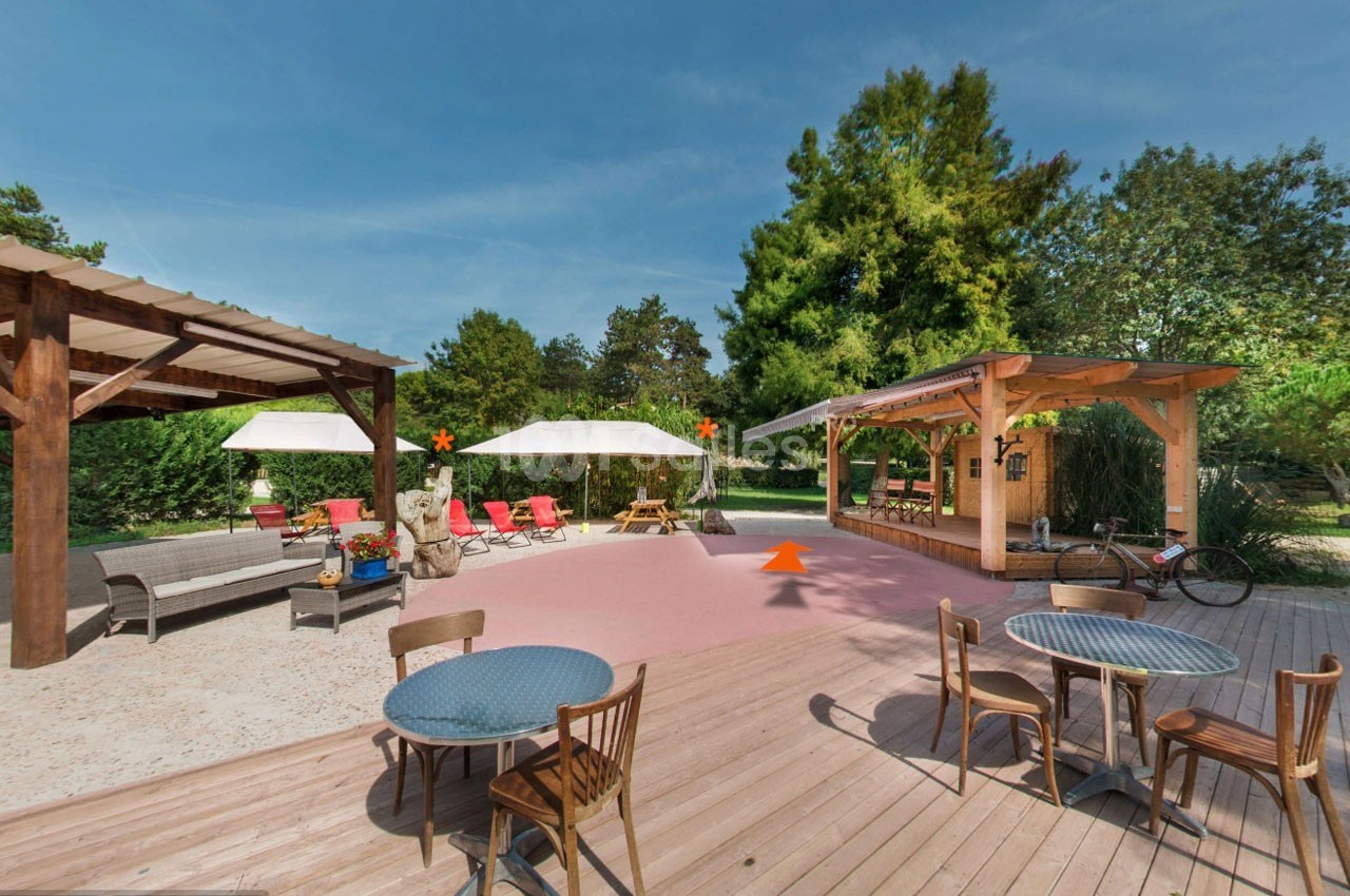 Terrasse extérieure avec tables, chaises, parasols, pergola en bois et végétation en arrière-plan.