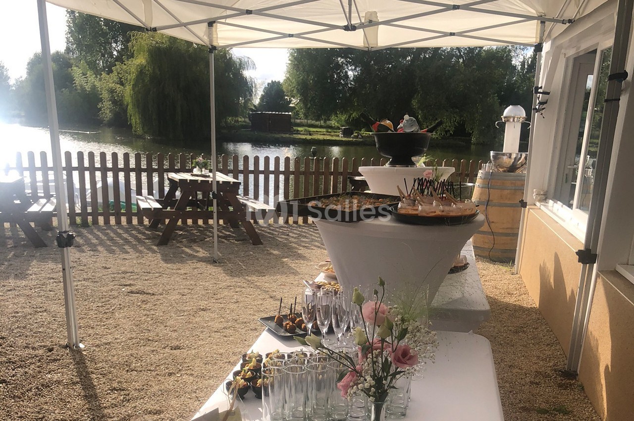 Buffet en plein air sous des tonnelles blanches, avec vue sur un étang et des tables de pique-nique en arrière-plan.