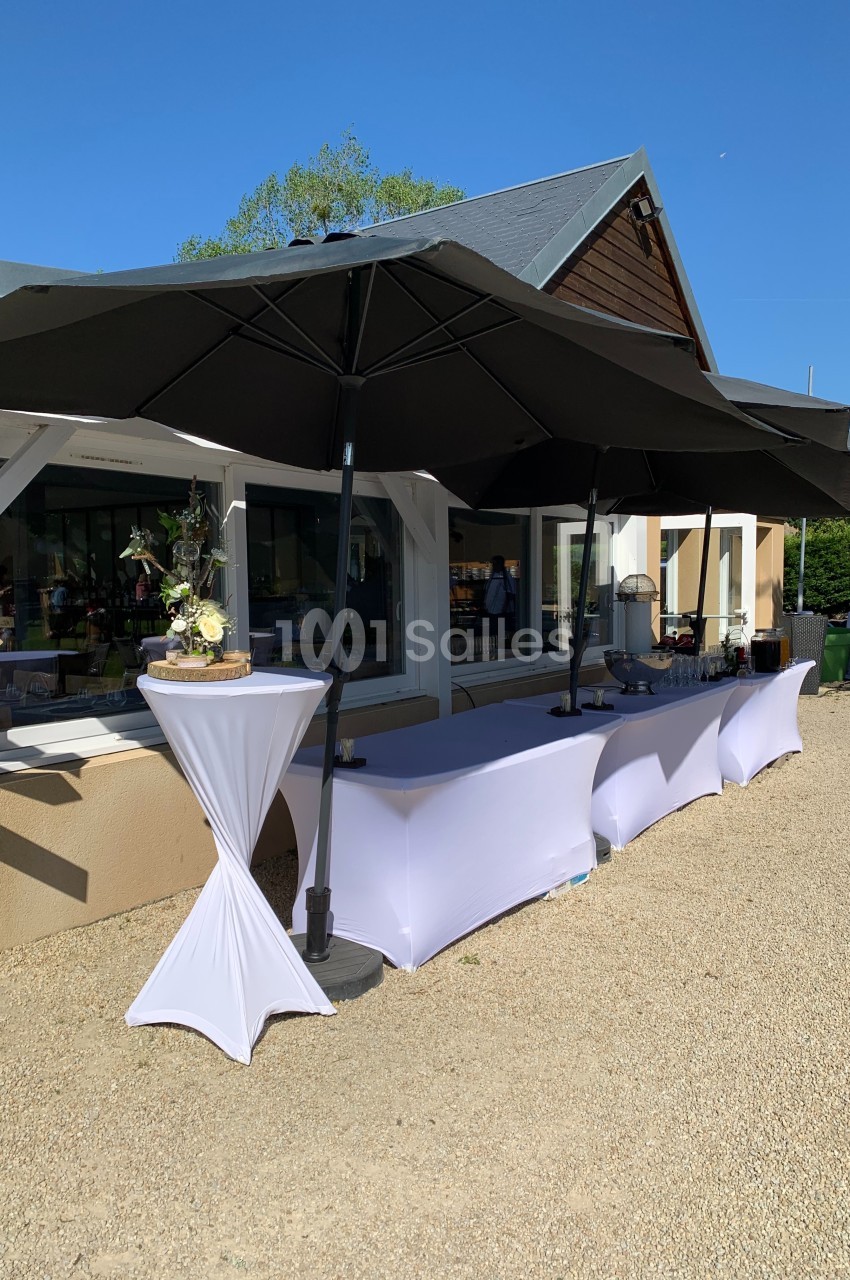 Table de buffet en extérieur, couverte de nappes blanches et protégée par de grands parasols noirs.
