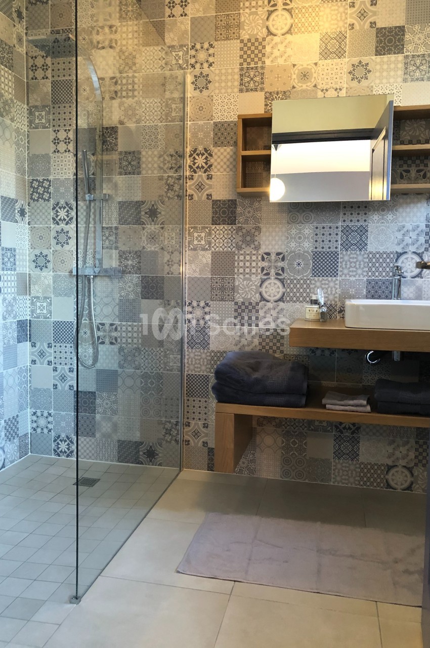 Salle de bain moderne avec douche à l'italienne, carreaux décoratifs, lavabo sur meuble en bois et miroir éclairé.