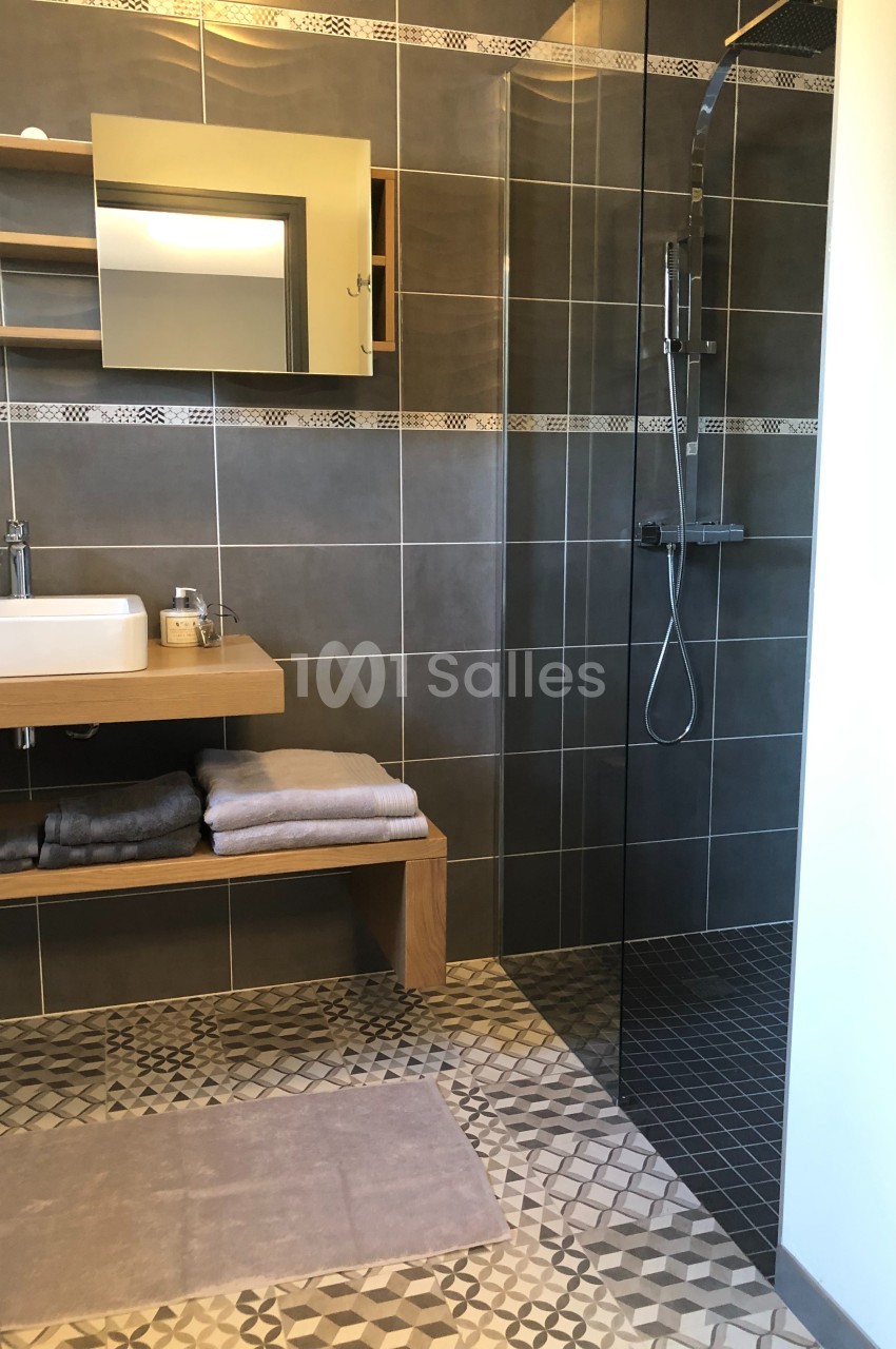 Salle de bain moderne avec douche à l'italienne, lavabo sur meuble en bois et serviettes pliées sur une étagère.