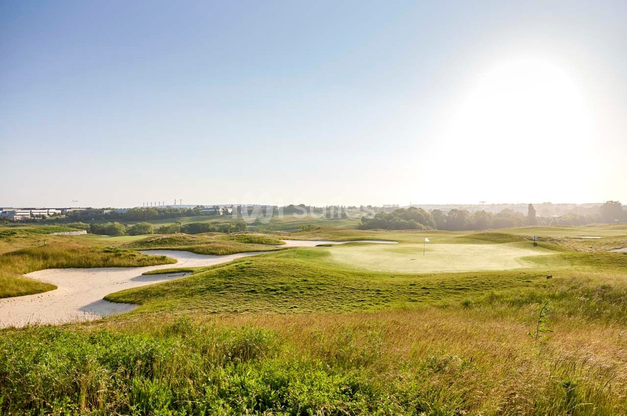 Paysage d'un terrain de golf verdoyant avec des bunkers de sable, sous un ciel dégagé et ensoleillé.