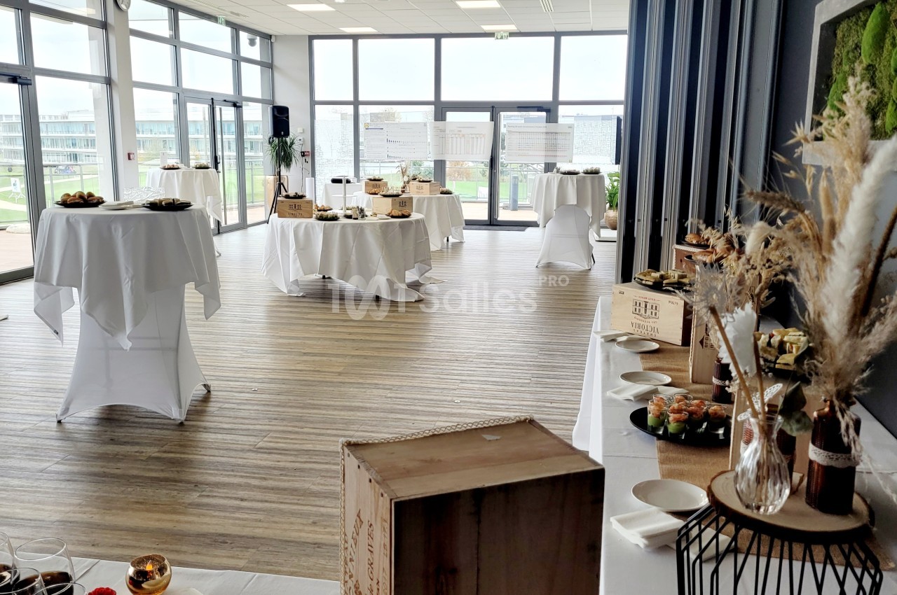 Salle lumineuse aménagée pour un buffet, avec tables nappées, plats variés et décoration végétale.