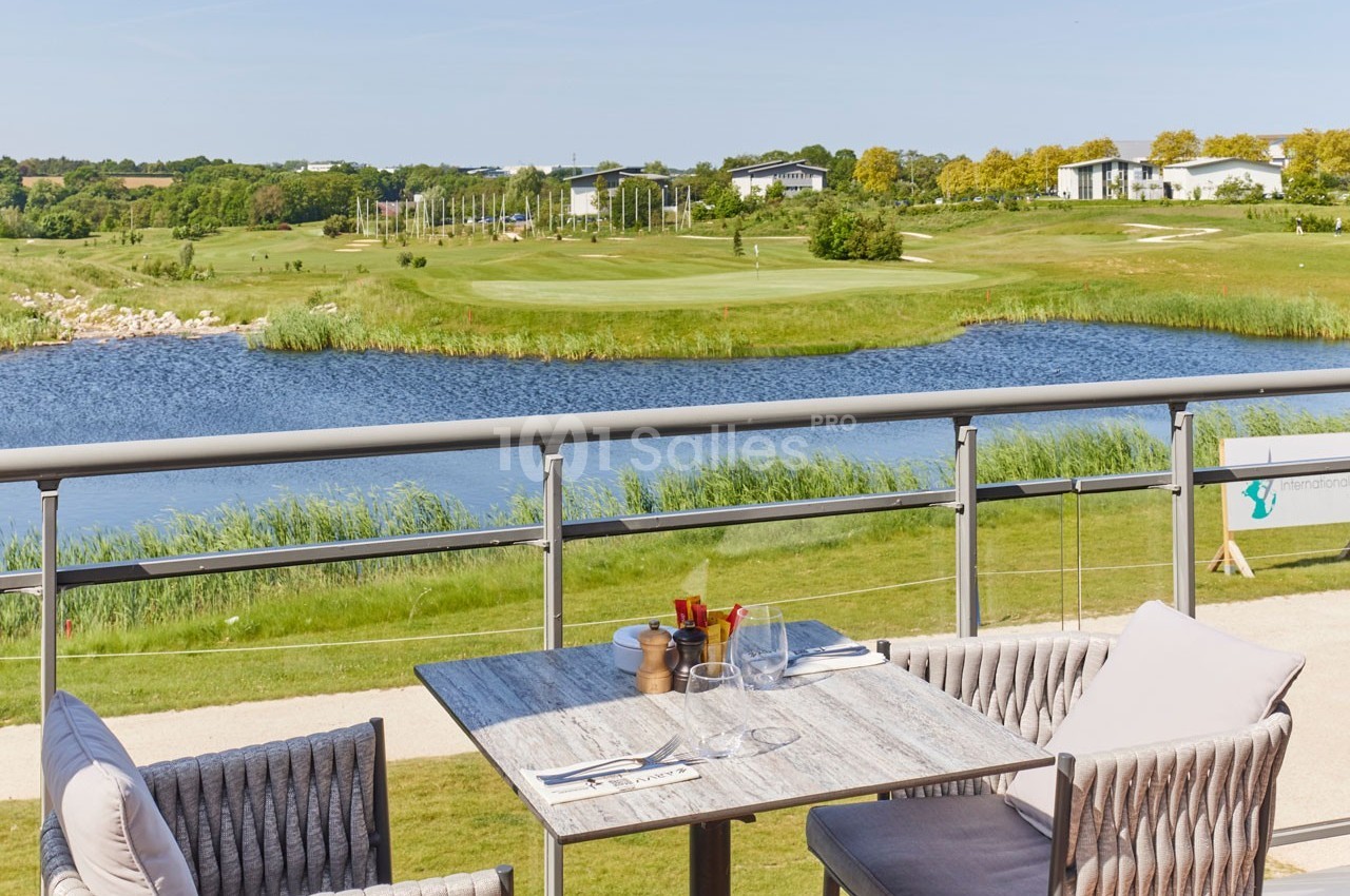 Vue d'une terrasse avec table et chaises donnant sur un parcours de golf, un lac et un paysage verdoyant.
