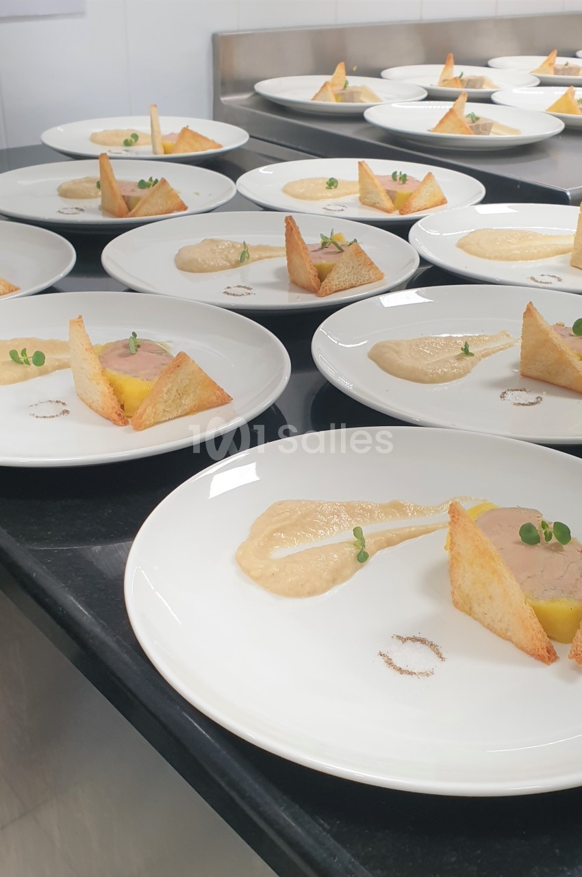 Assiettes dressées avec foie gras, toasts triangulaires, purée et micro-pousses sur un plan de travail en cuisine.
