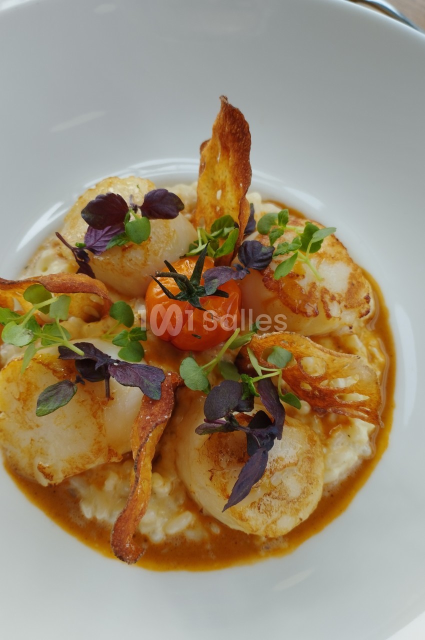 Assiette de noix de Saint-Jacques sur risotto crémeux, garnie de chips croustillantes, herbes fraîches et tomate cerise.