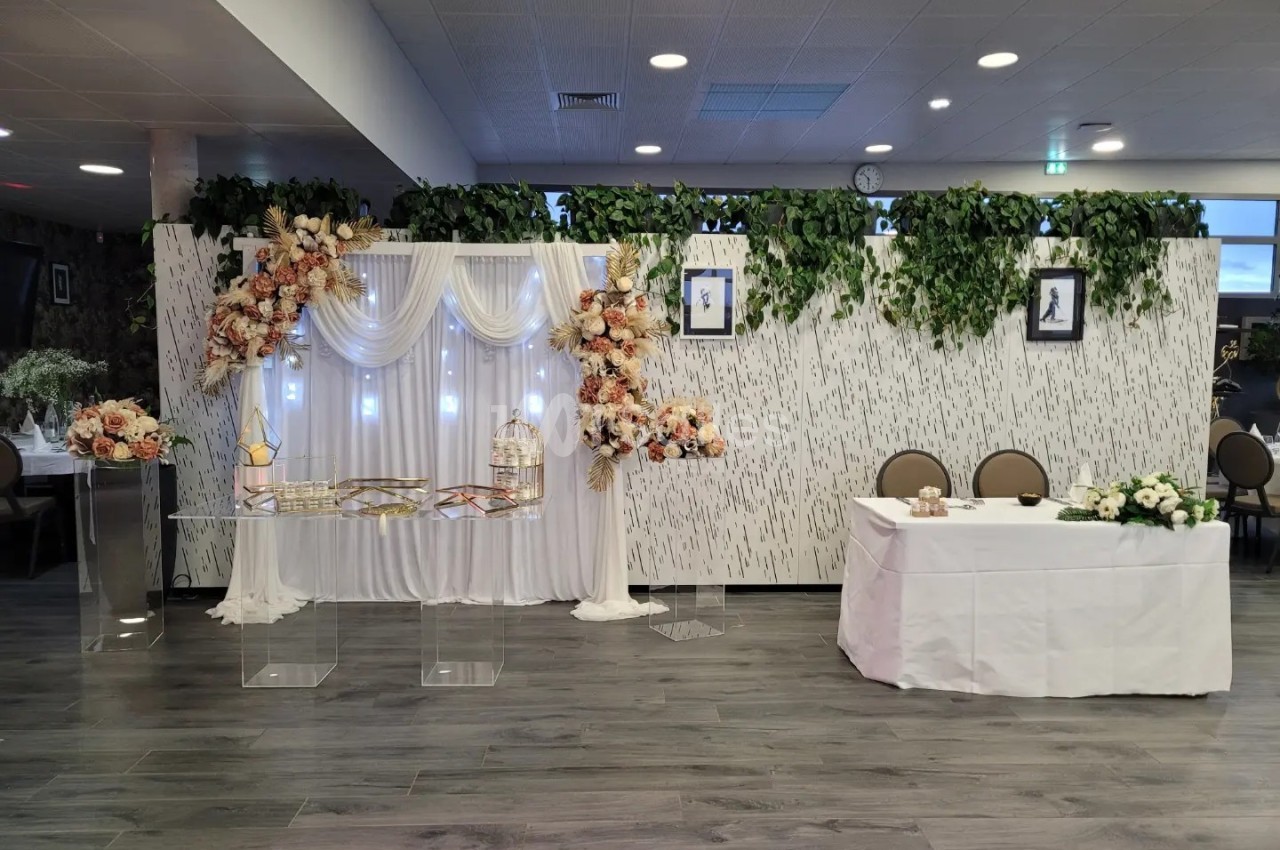 Décoration de salle avec un mur végétalisé, une arche florale lumineuse, et une table ornée de fleurs blanches.