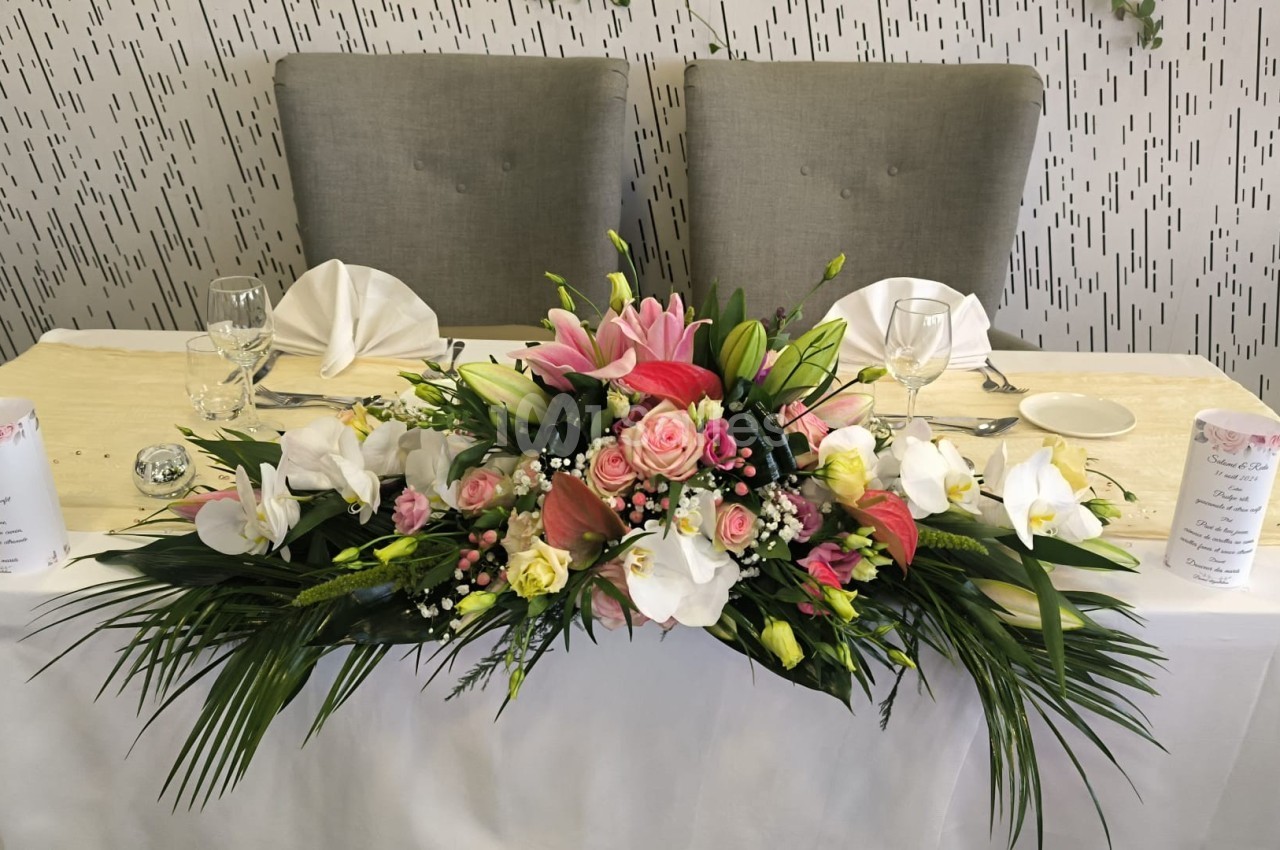Arrangement floral coloré avec des roses, lys et feuillages, décorant une table blanche dressée pour un événement.