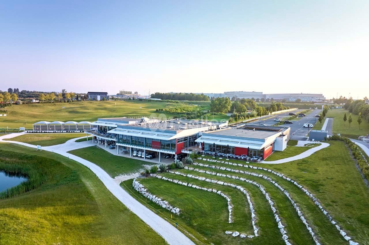Vue aérienne d'un bâtiment moderne entouré de pelouses, d'allées et d'un espace paysager avec gradins en pierre.