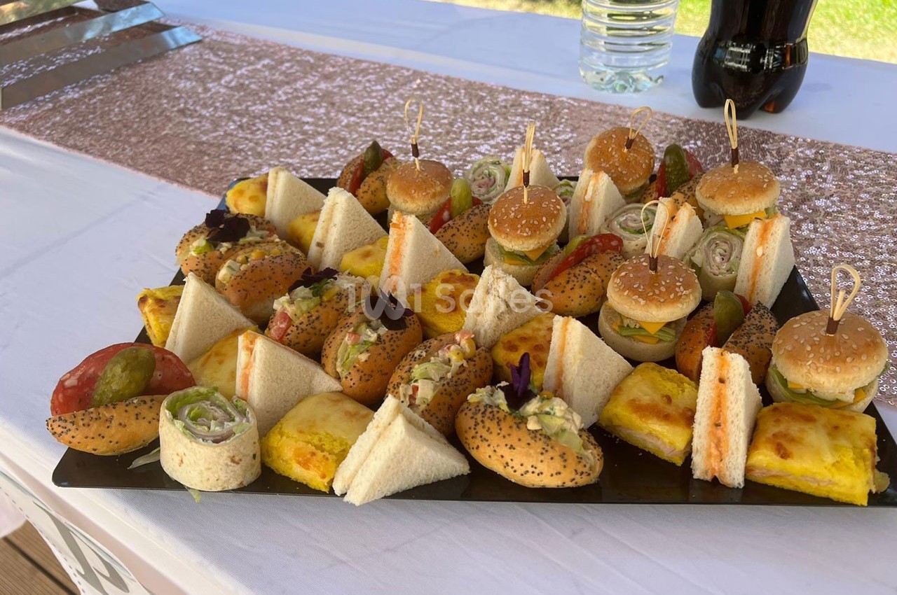 Plateau de mini-sandwichs variés, roulés, triangles et bouchées salées, présenté sur une table décorée.