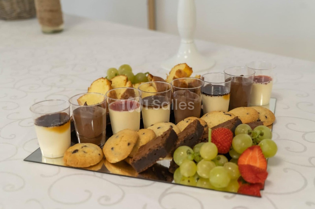 Plateau de desserts variés comprenant verrines, cookies, brownies, raisins et fraises, disposé sur une table blanche.