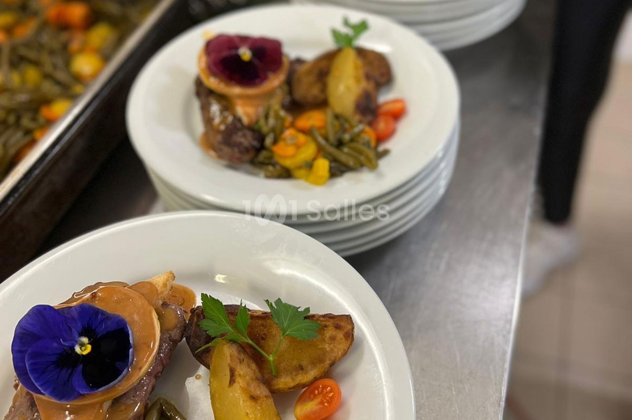 Assiettes garnies de viande, légumes verts, pommes de terre et fleurs comestibles, servies sur un plan de travail.