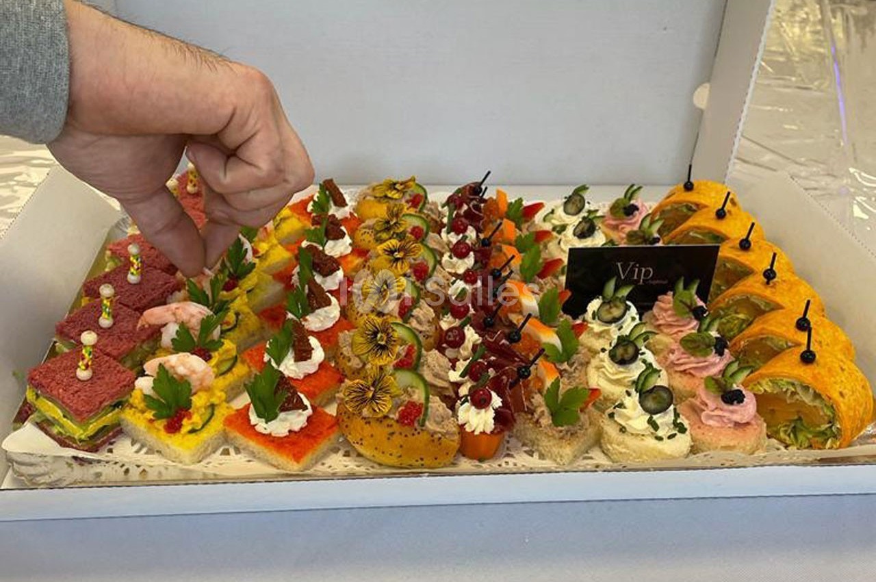 Plateau de canapés variés colorés, garnis de légumes, fruits et herbes, avec une main ajustant une décoration.