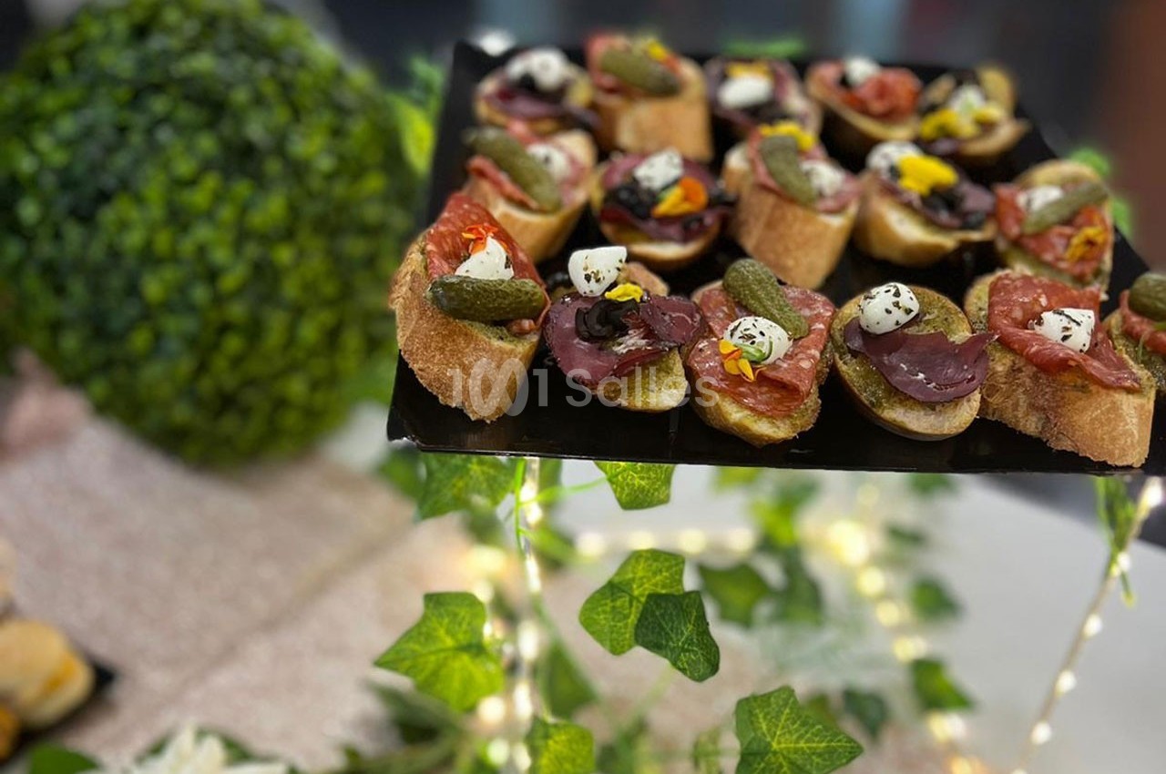 Plateau de canapés variés garnis de charcuterie, cornichons et fromage, présenté sur une table décorée de verdure.